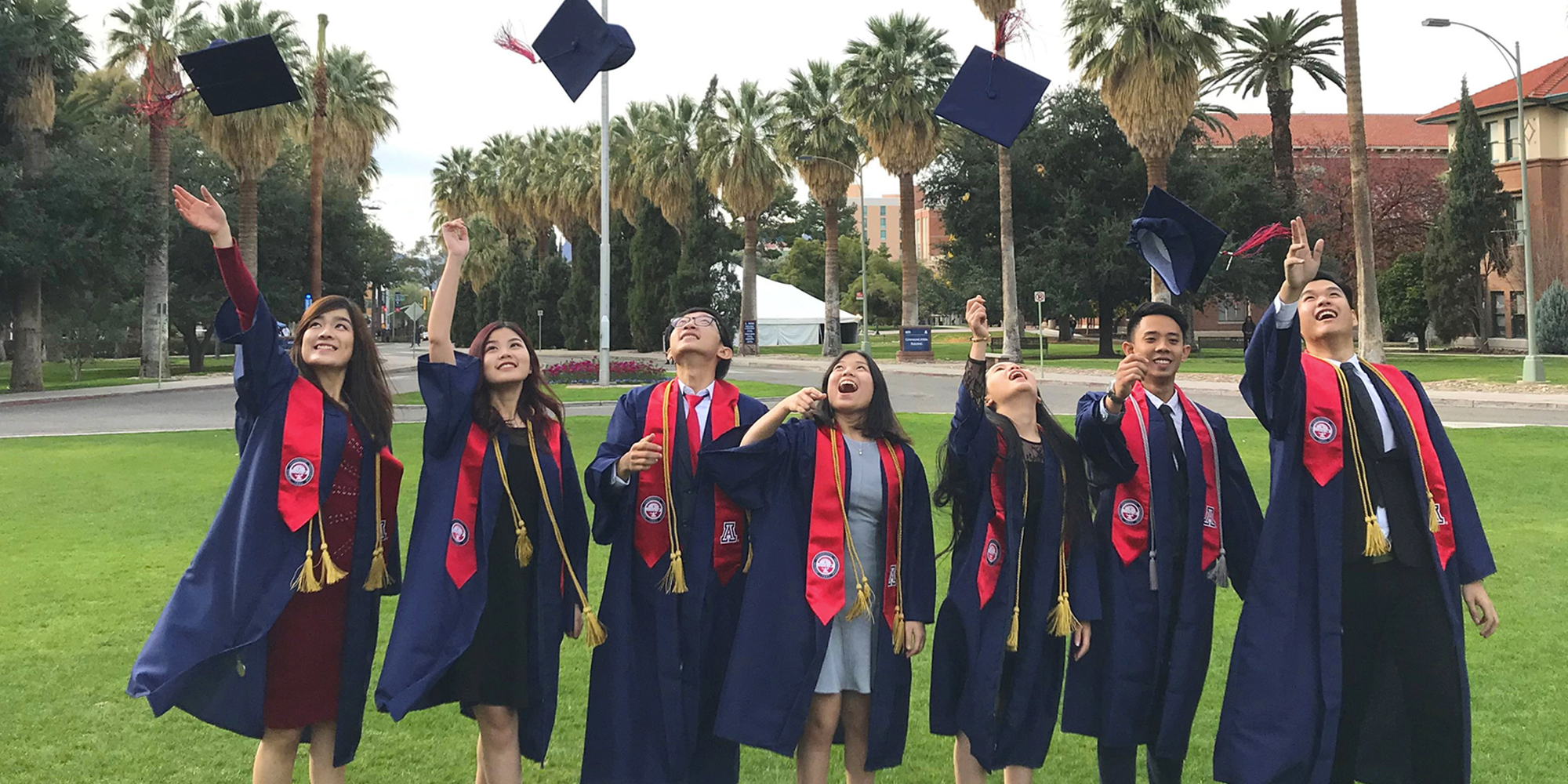 Seven International Dual Degree students at  UArizona wearing graduation gowns and throwing their graduation caps into the air
