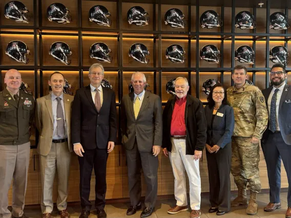 United States Ambassador to Kazakhstan Daniel Rosenblum stands with state and university officials in front of a wall of football helmets.