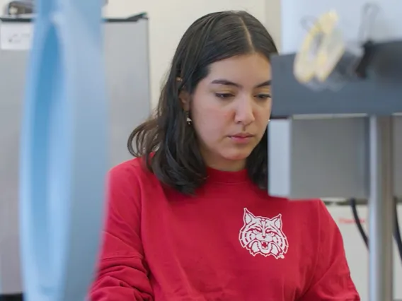 UArizona student Sam sits in front of a microscope