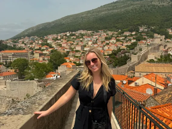 Kylie stands on a bridge with Dubrovnik, Croatia behind her