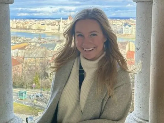 Kylie sits in a window with the city of Budapest, Hungary behind her.