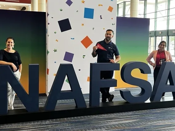 Three AZI staff members standing behind large letters spelling NAFSA