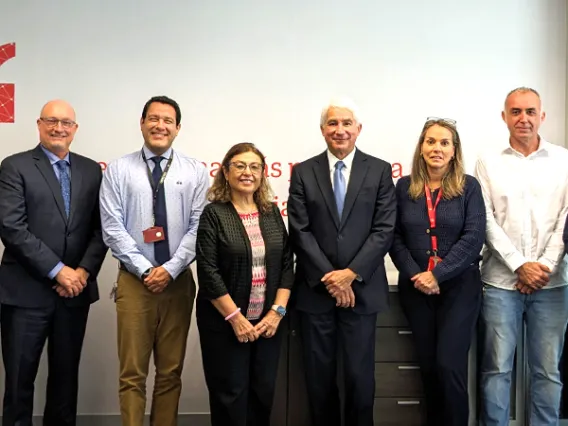 Leadership from UPC and UArizona are standing in a row, smiling at the camera. They are dressed in business attire, ranging from suits and ties to business casual clothing. The background features a white wall with red text and symbols.