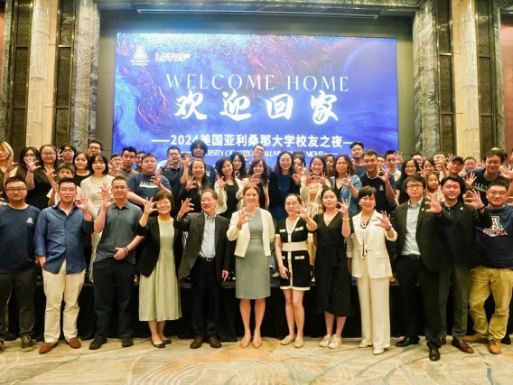 The U of A Chinese Alumni Club stands in front of a welcome slide.