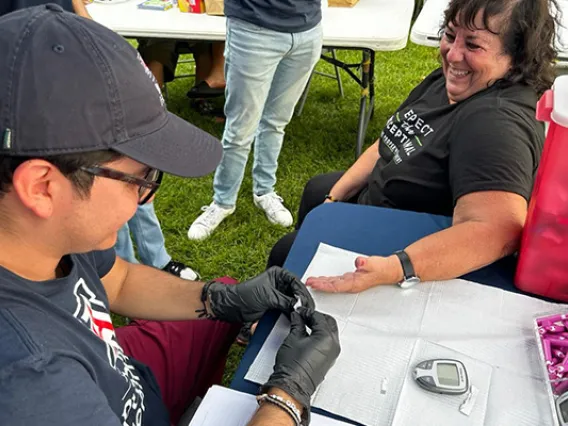 Student sits at a table helping a smiling woman.