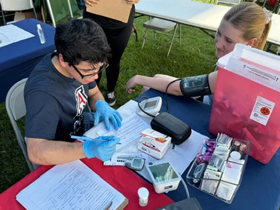 Student sits a table taking the blood pressure of another student.