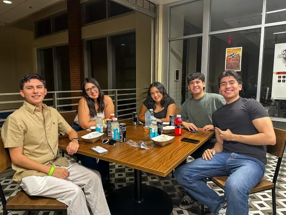 Students smiling at the camera while sitting at a table.