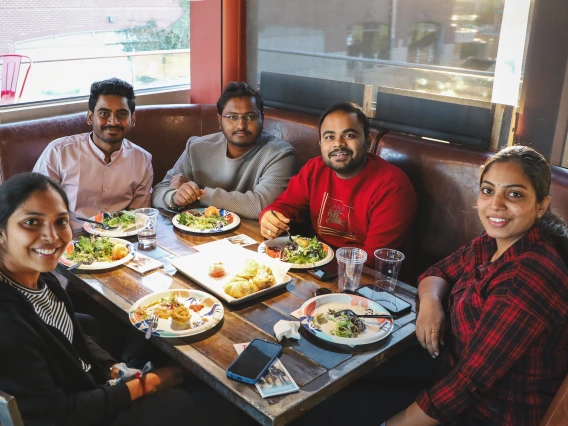 U of A international students sit at a table and smile at the camera