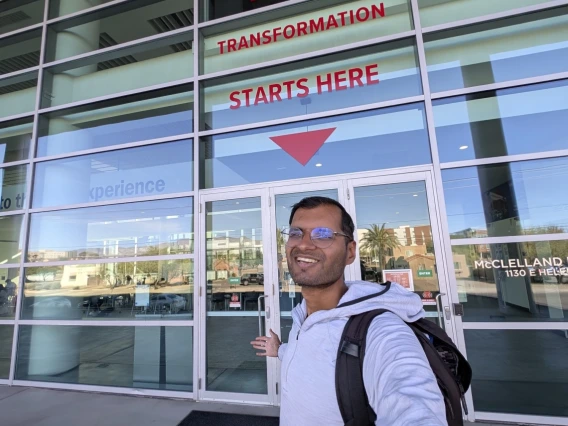 Shreyas in front of a sign reading "Your Transformation Starts Here." 