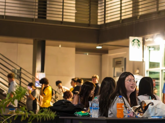 Students gather at outdoor tables in the evening near the Starbucks at the University of Arizona Global Center during a campus event, with drinks, snacks, and conversations creating a lively atmosphere.