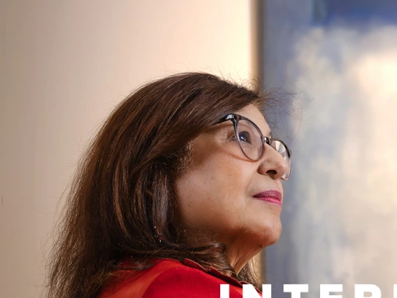 Dr. Iman Hakim, dean of the University of Arizona Mel and Enid Zuckerman College of Public Health, looks thoughtful while gazing upward. She is wearing glasses and a red outfit, with the words "International Exchange" displayed in bold white text beside her.