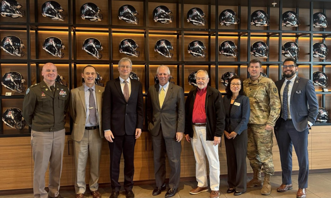 United States Ambassador to Kazakhstan Daniel Rosenblum stands with state and university officials in front of a wall of football helmets.