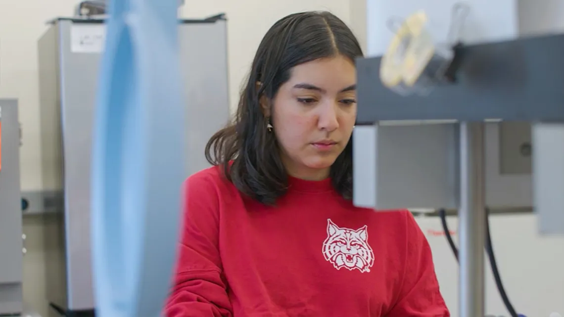 UArizona student Sam sits in front of a microscope