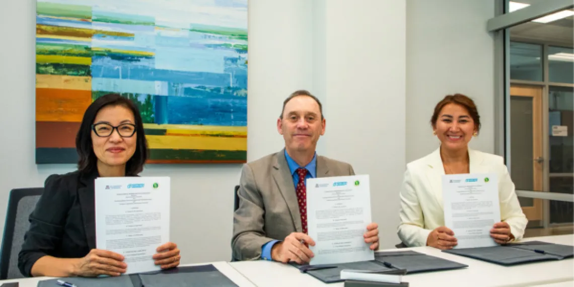 Three individuals hold up signed meemorandums