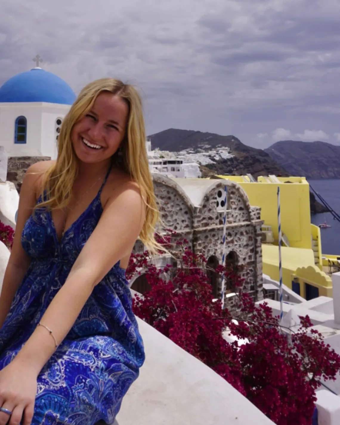 Kylie sitting on a wall with the city of Santorini, Greece behind her