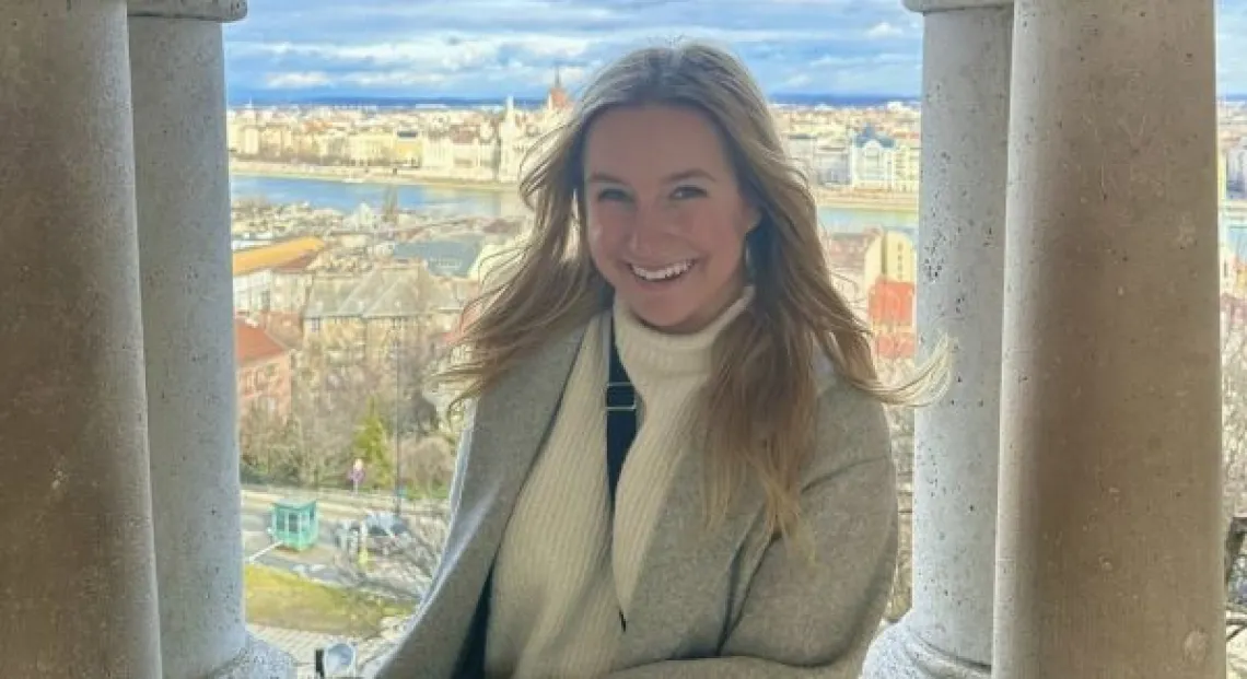 Kylie sits in a window with the city of Budapest, Hungary behind her.