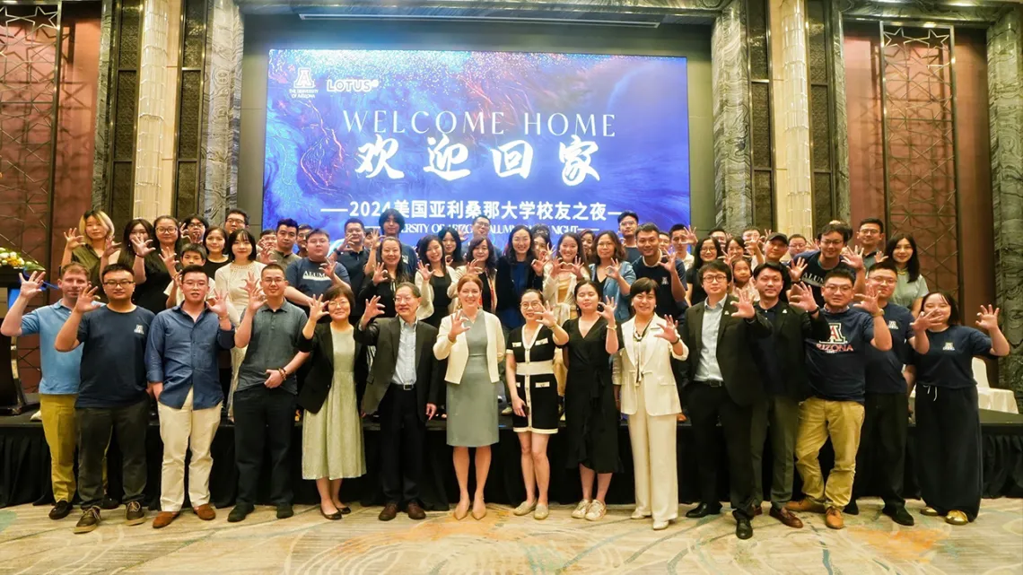 The U of A Chinese Alumni Club stands in front of a welcome slide.