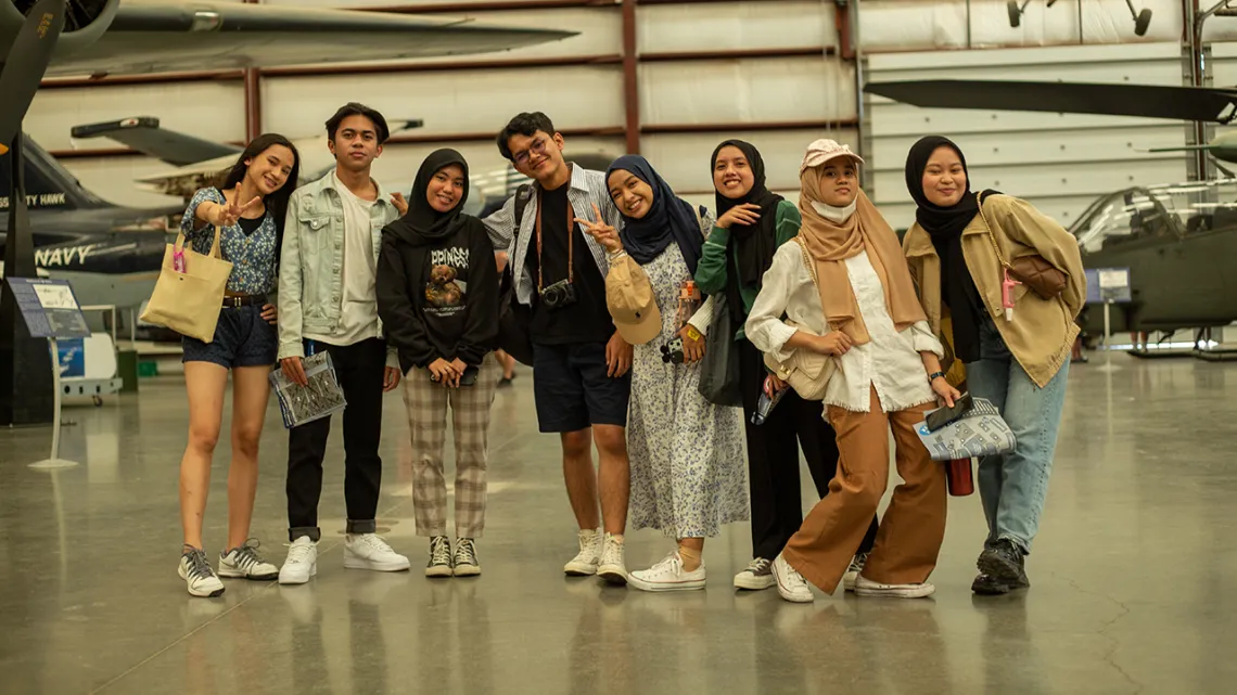 A group of students smile at the camera with airplanes behind them.