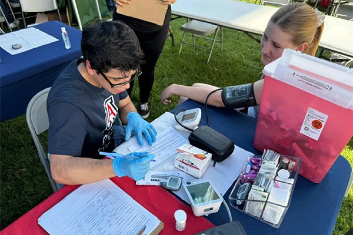 Student sits a table taking the blood pressure of another student.