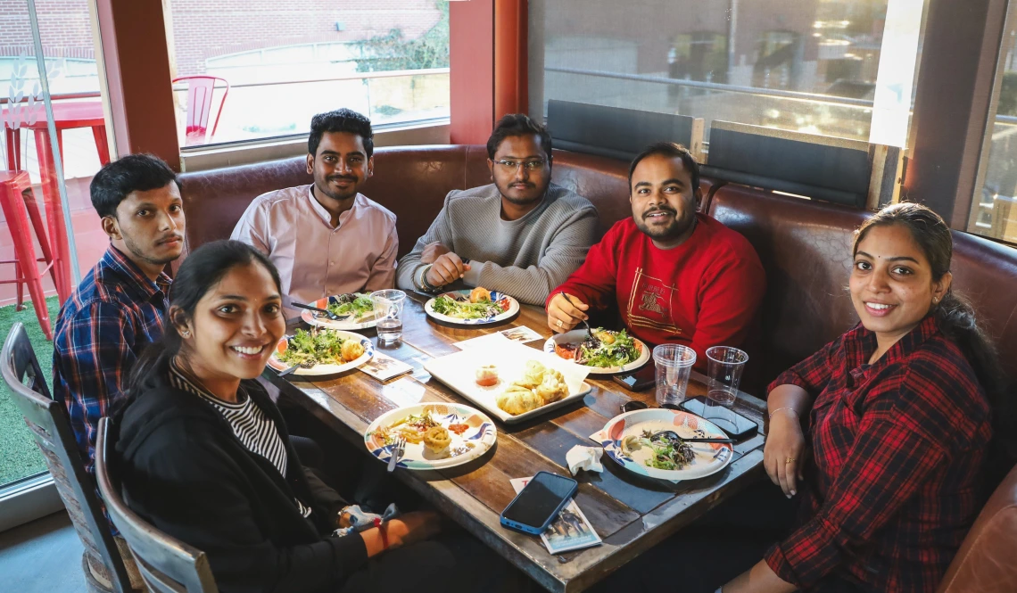 U of A international students sit at a table and smile at the camera