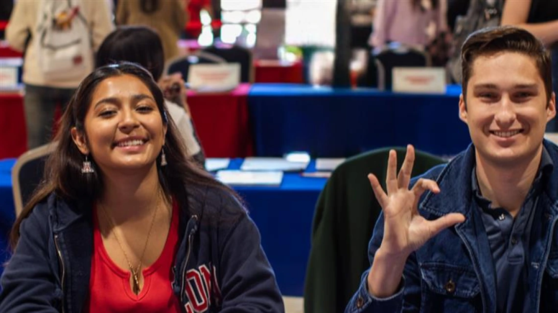 Students smiling at the camera while sitting at a table.