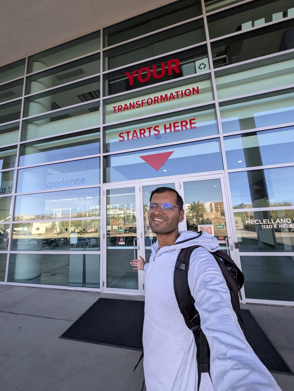 Shreyas in front of a sign reading "Your Transformation Starts Here." 