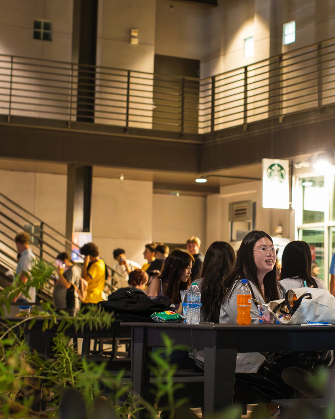 Students gather at outdoor tables in the evening near the Starbucks at the University of Arizona Global Center during a campus event, with drinks, snacks, and conversations creating a lively atmosphere.