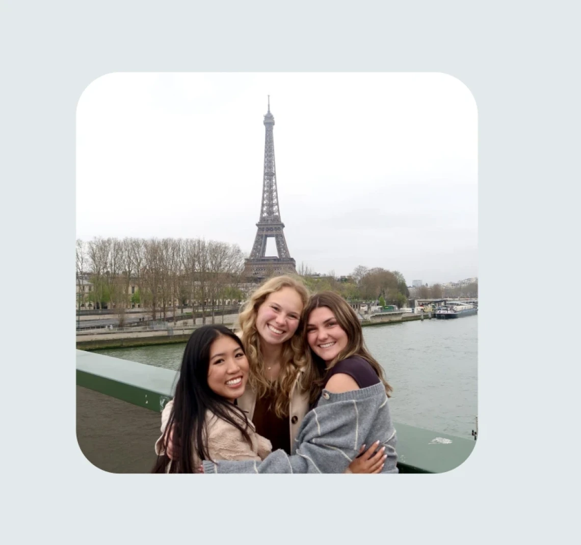 Three students hug in front of the Eiffel Tower.