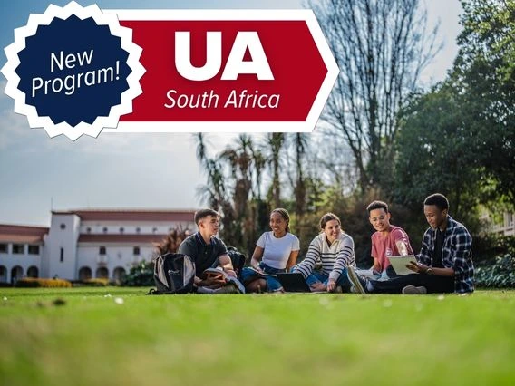 Five students sit on the lawn studying on a university campus