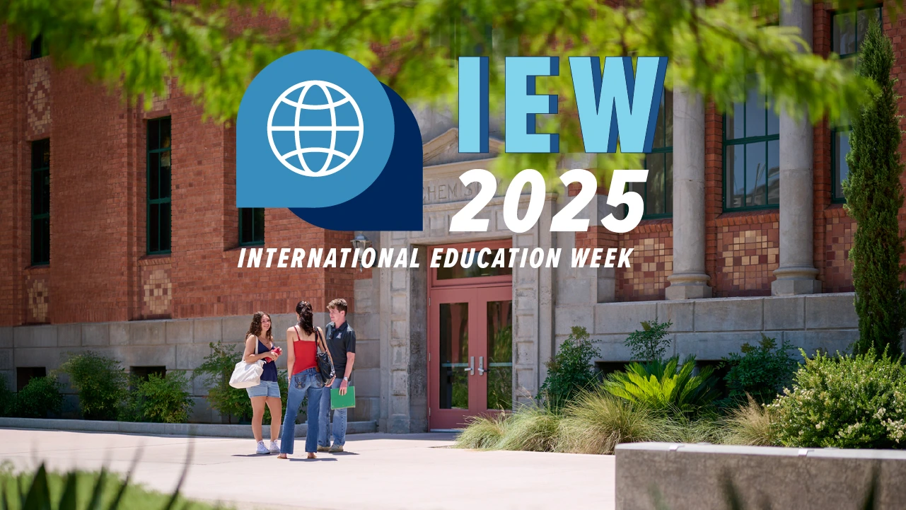Three students stand talking in front of a historic brick building on the University of Arizona campus, with green trees and plants around them. Overlaid text reads “IEW 2025 International Education Week” with a blue globe logo.