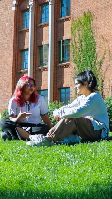 UArizona student Adiba sits outside on grass with a friend.