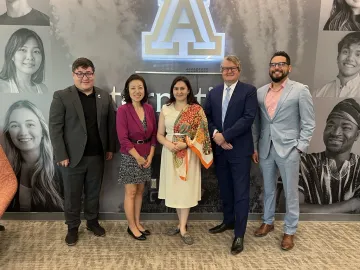 Kozybayev University and UArizona officials stand in front of a wall of student images.