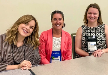 Three women sit together at a conference panel table, smiling for the camera during a NAFSA session. They are wearing conference badges and business casual attire, appearing engaged and enthusiastic about their participation.