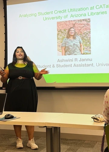Ashwini R. Jannu gives a presentation titled “Analyzing Student Credit Utilization at CATalyst Studios, University of Arizona Libraries,” standing in front of a projector screen displaying her name and photo.
