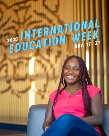A smiling student with long braided hair, wearing a bright pink top and jeans, sits on a chair in front of a warmly lit decorative wooden backdrop. Bold blue text above her reads: "2025 International Education Week, Nov. 17–21."