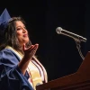 Ashwini R. Jannu, MSIS ’25, delivers the graduate student speech at the Spring 2025 College of Information Science Convocation. Wearing a cap and gown with a gold stole and honor cords, she gestures expressively while speaking into a microphone from behind a podium. Jannu was honored as the Outstanding Graduate Student award-winner.