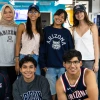 Eight students pose together indoors, all wearing University of Arizona apparel, including shirts, sweatshirts, and hats. Five students stand in the back row, and three kneel in the front, smiling at the camera. The background features a brightly lit lounge area with blue seating and a “Campus Recreation” sign.