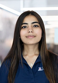 Alt text: Portrait of Aariya, a University of Arizona Global Ambassador, wearing a navy U of A polo shirt and smiling slightly while standing indoors with blurred background lighting.