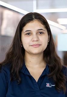 Catalina, a Global Ambassador at the University of Arizona, wearing a navy Arizona International polo shirt, smiles softly at the camera in an indoor setting with blurred background lighting.