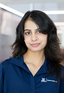 Portrait of Navya, a Global Ambassador at the University of Arizona, wearing a navy blue Arizona International polo, smiling softly with dark hair framing her face in a bright indoor setting.