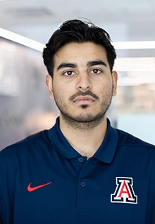 Redwan, a Global Ambassador at the University of Arizona, wearing a navy blue polo shirt with the red and white block "A" logo, poses indoors against a softly blurred background.