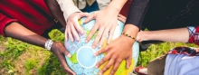 Closeup of hands of diverse skin colors holding a large globe of the world