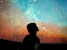 Nikhil Garuda in shadow profile standing in front of a large photo of the sky and stars