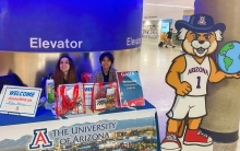 two female Global Ambassadors Wildcat Welcome table at Tucson Airport with Wilbur Wildcat