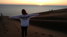Student wearing white wildcats shirt on beach at sunset