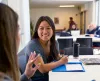 A female student smiles as another student talks to her.