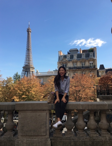 UA Study Abroad Student Stephanie Kim sitting on a wall in Paris with the Eiffel Tower in the background.