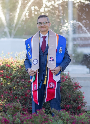 Jiten stands near Old Main fountain, wearing his many graduation and honor stoles 
