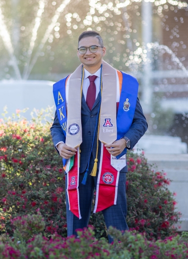 Jiten stands near Old Main fountain, wearing his many graduation and honor stoles