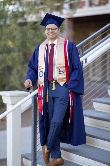 Jiten is wearing full graduation regalia and standing at the step near Old Main